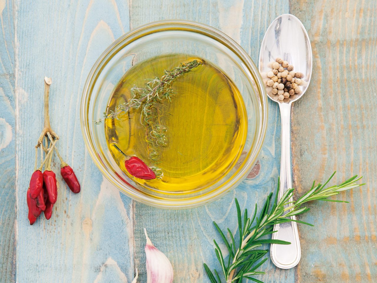 Ein Glas Olivenöl mit einem silbernen Löffel daneben 