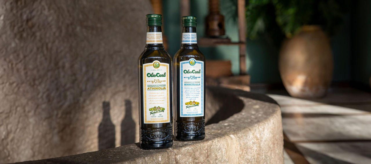 due bottiglie di evo Carli appoggiati su mulino in pietra